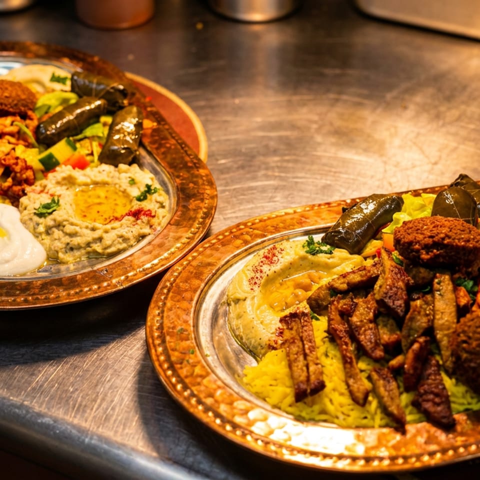 Two copper platters overflowing with Middle Eastern food, including falafel, shawarma, rice, hummus, and yogurt sauce.